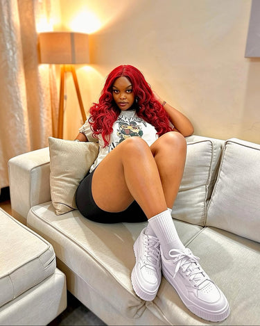 A woman with vibrant red hair sits on a light beige sofa, wearing a white graphic t-shirt, black shorts, white crew socks, and white platform original and authentic PUMA sneakers from Kicks Kenya.
Kicks Kenya has grown to be the premium multi-brand store in East Africa.